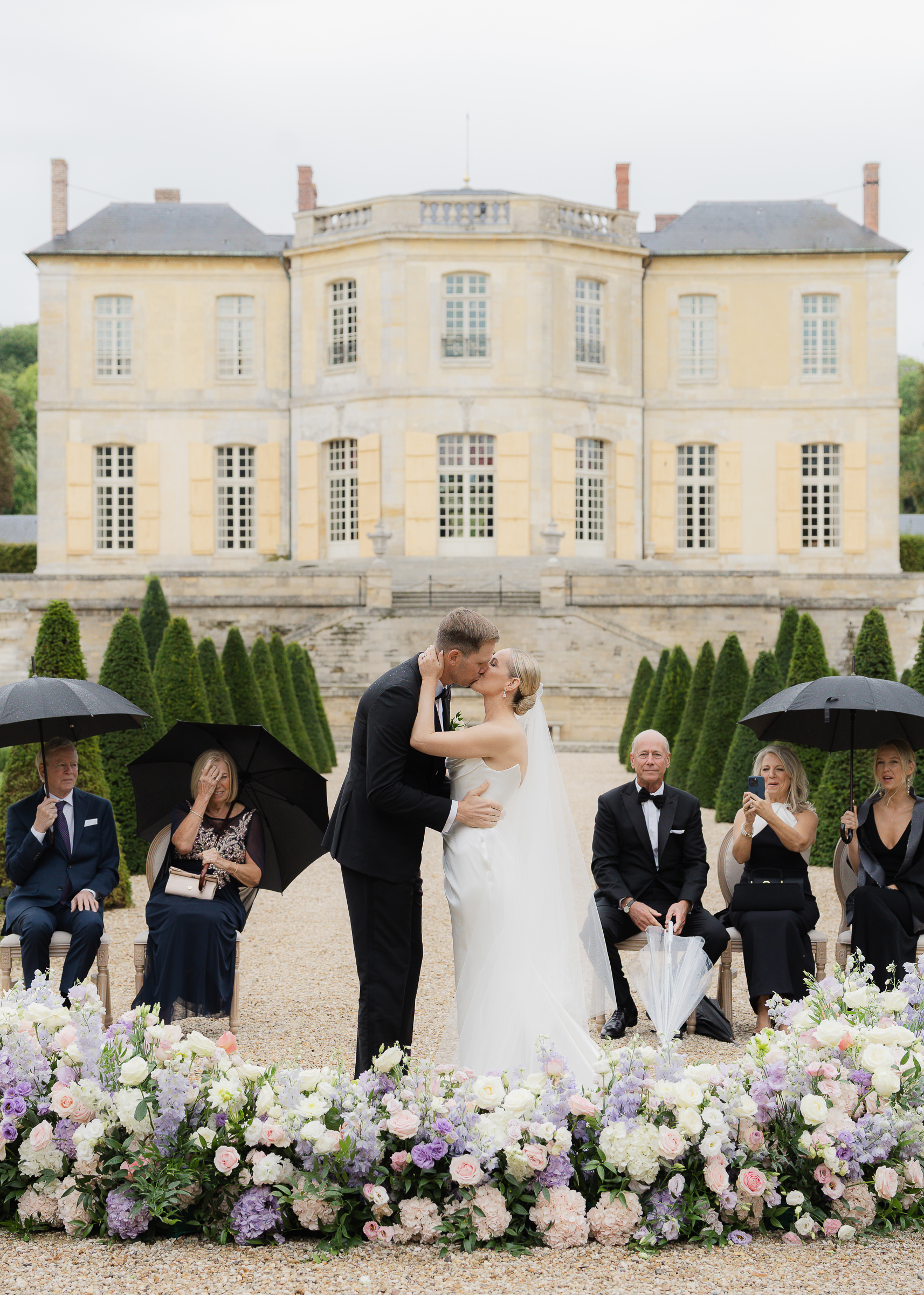 Guests holding umbrellas during an intimate first kiss at Château Villette wedding ceremony