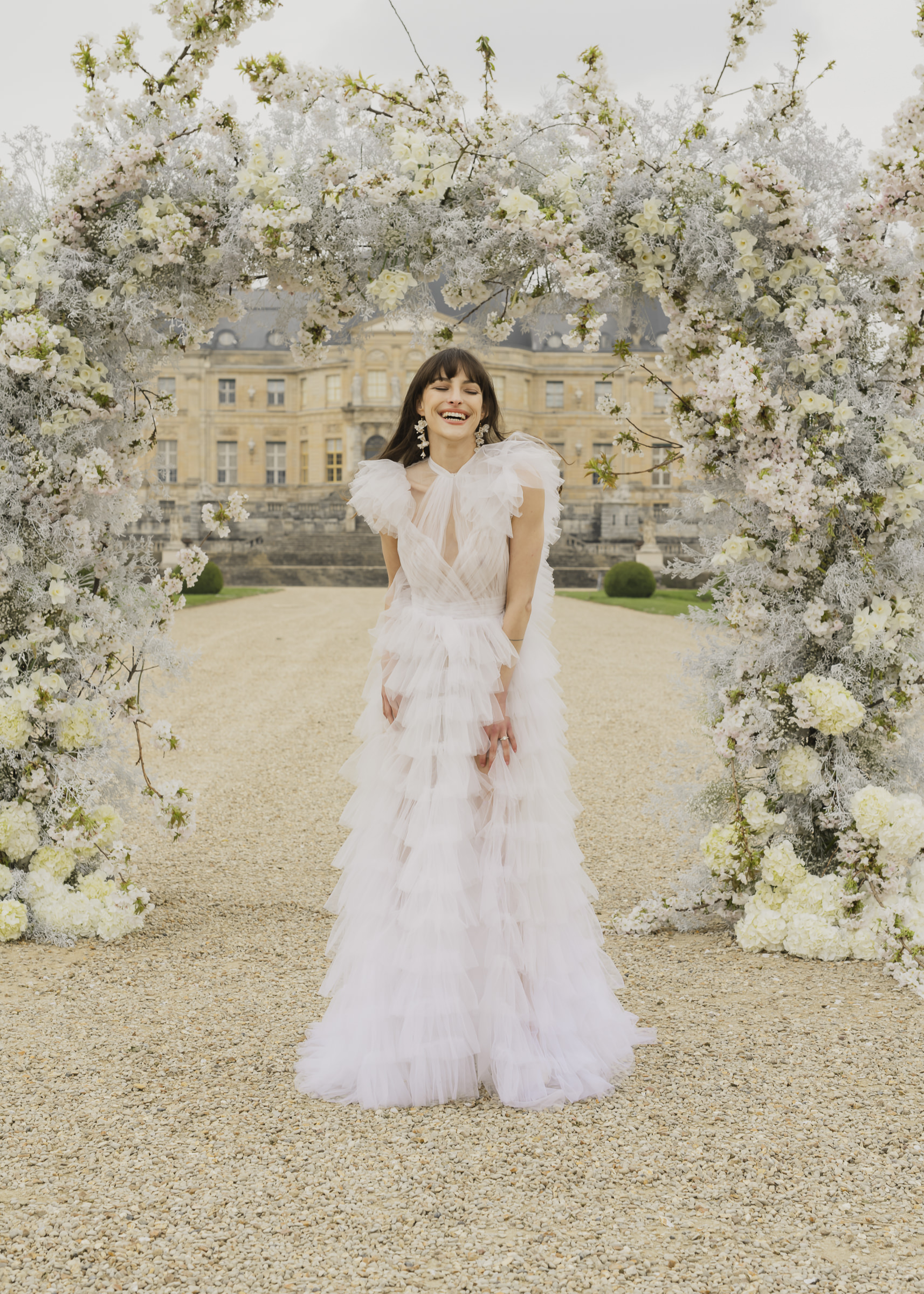 Bride laughing posed beneath the ceremony flower arch at Château de Vaux-le-Vicomte