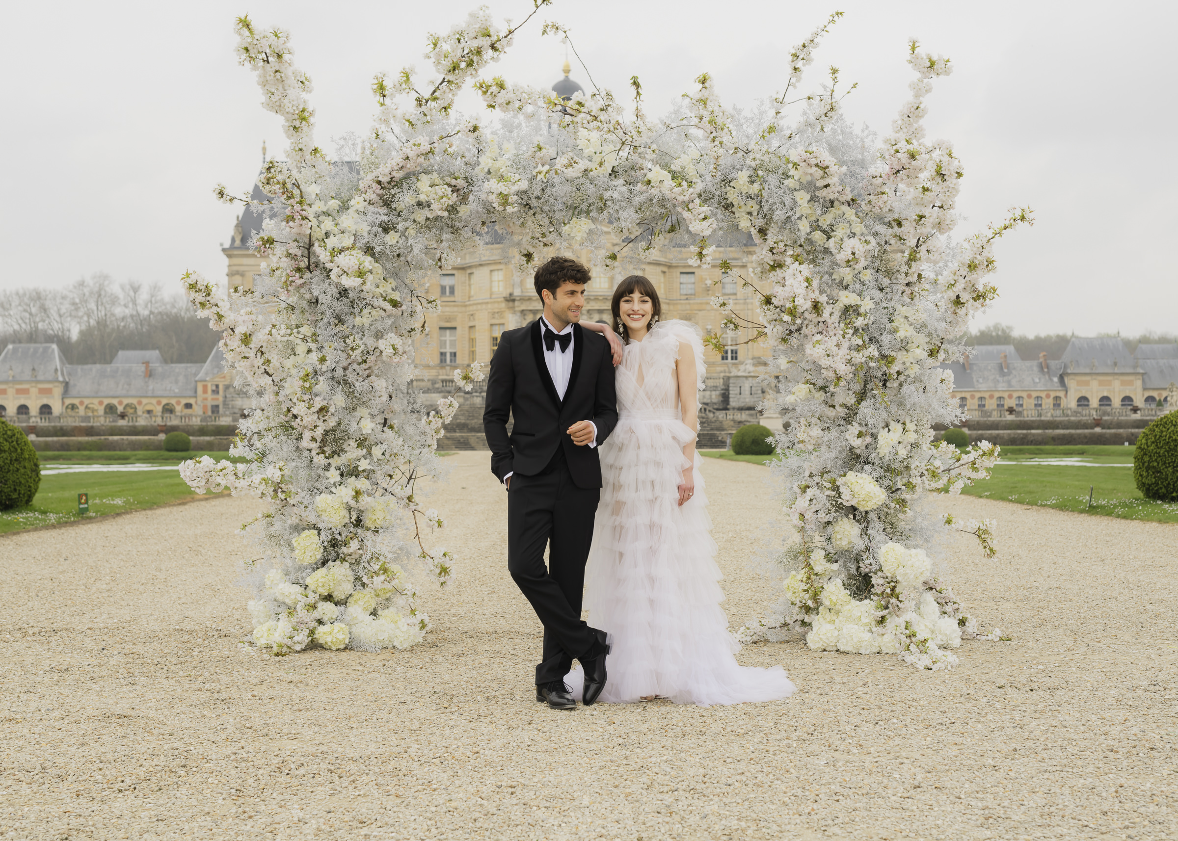 Bride and groom posed beneath the ceremony flower arch at Château de Vaux-le-Vicomte
