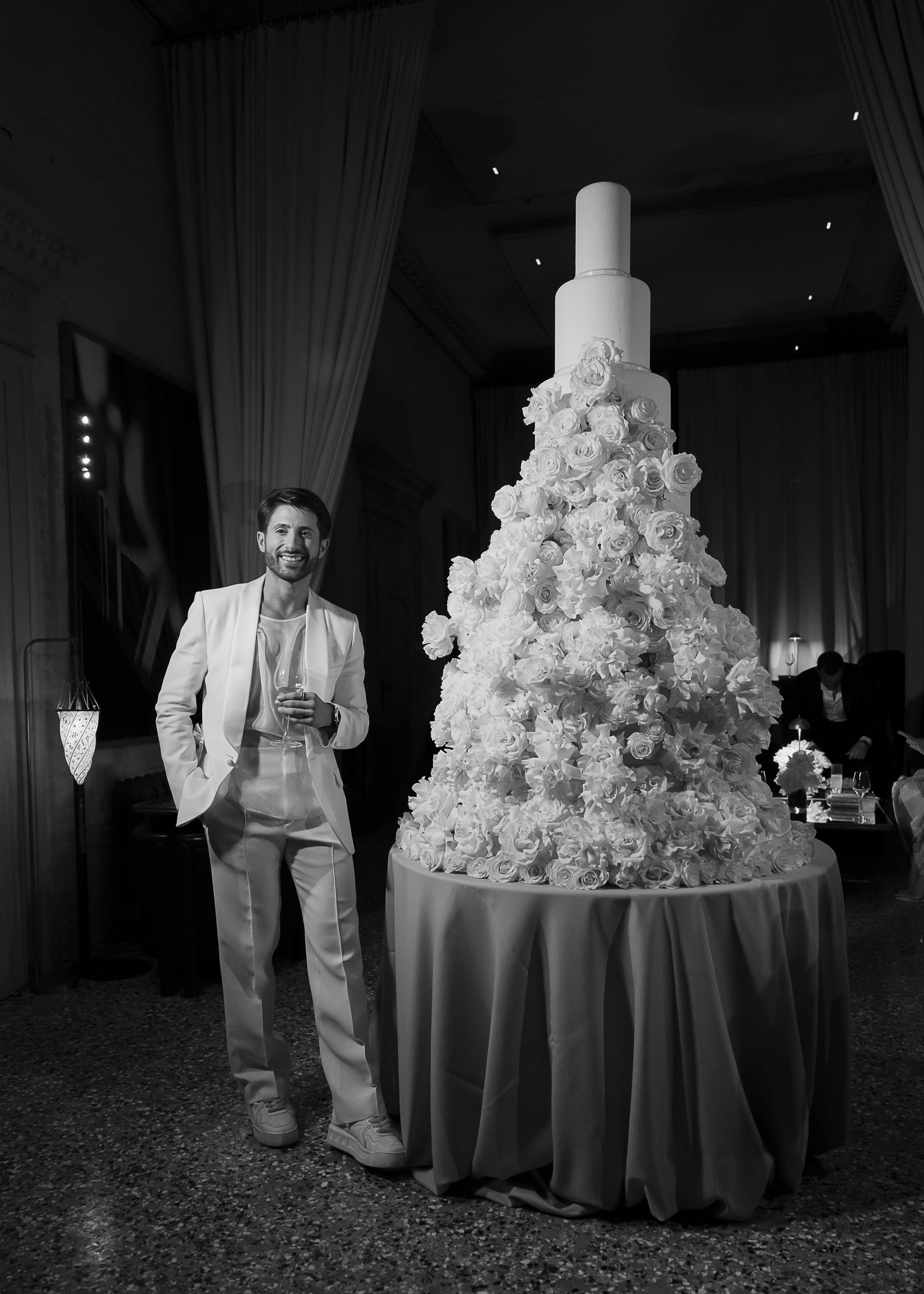Guest of honour with a towering cake adorned with white flowers in Venice
